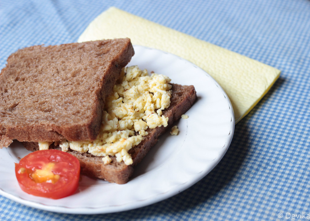 Scrambled egg sandwich on brown bread with a tomato slice