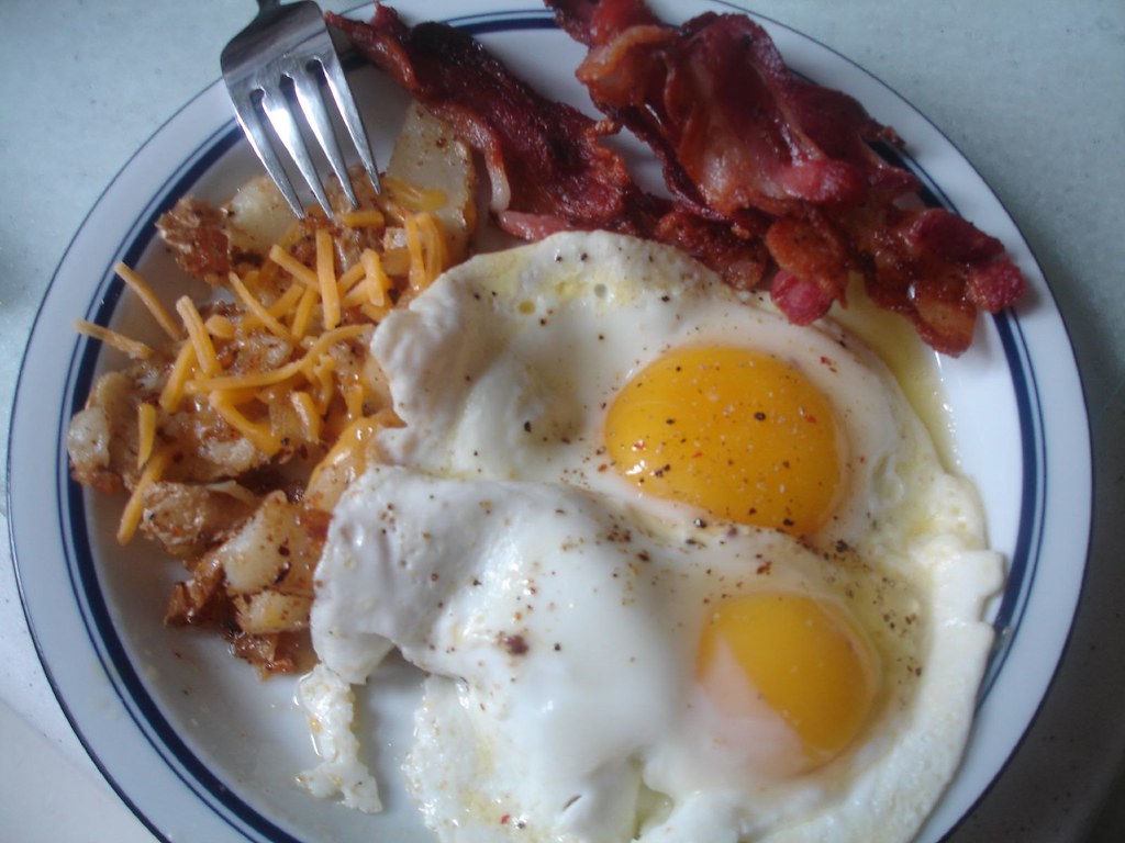 Two fried eggs with bacon and home fries on a white plate