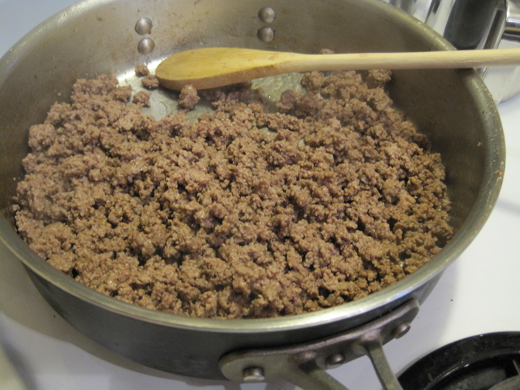 Cooked ground beef in a skillet with a wooden spoon