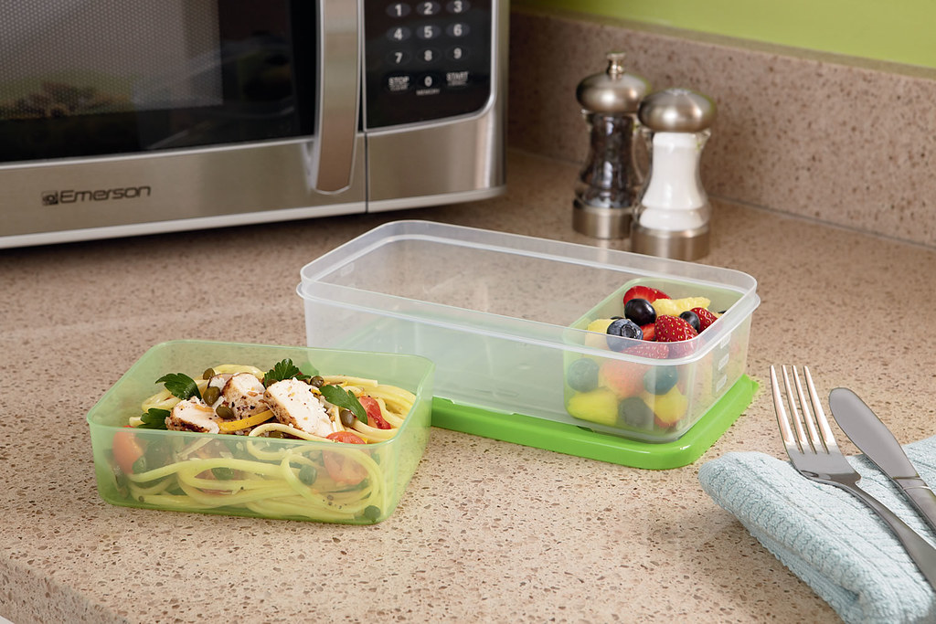 Plastic lunch containers with pasta and fruit on a kitchen counter