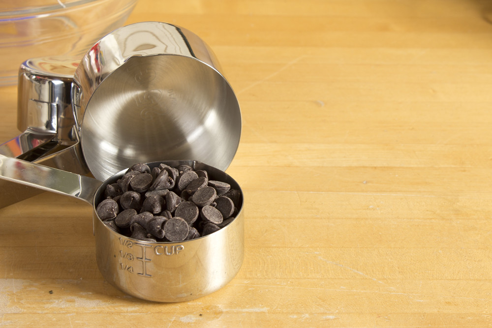 Chocolate chip ingredient in a metal measuring cup on a wooden counter