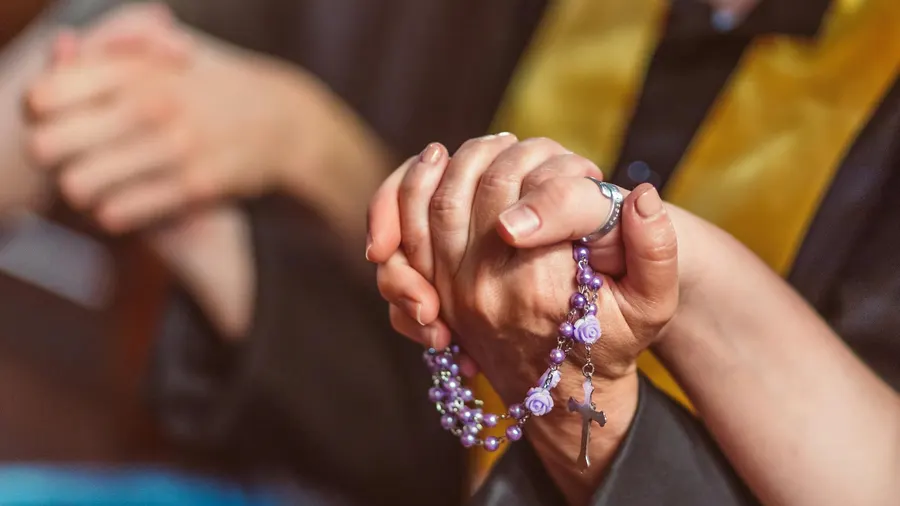 Mãos dadas com um terço em contexto de oração comunitária