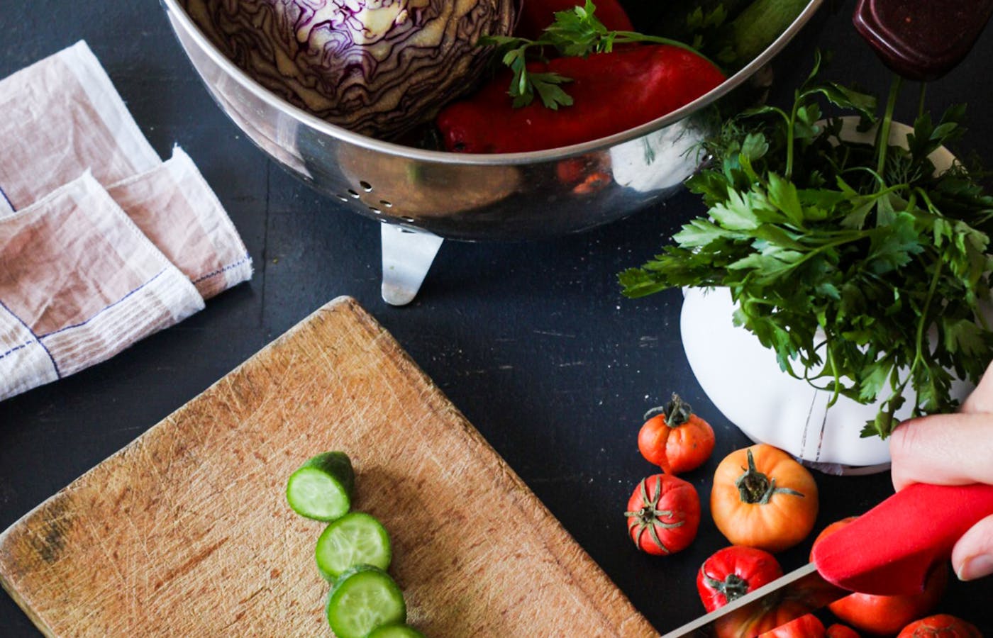 Meal prep vegetables and herbs on a kitchen counter while a red pepper is sliced