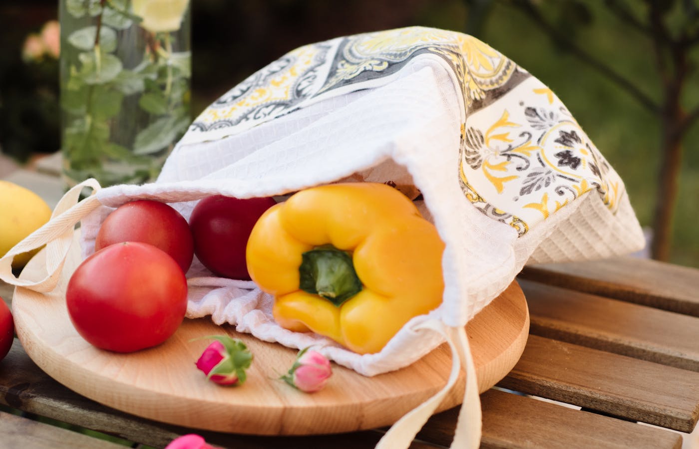 Tomatoes and a yellow bell pepper spilling from a cloth grocery bag on a table