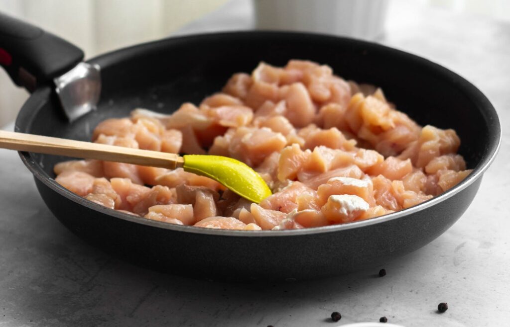 Raw diced chicken cooking in a black skillet