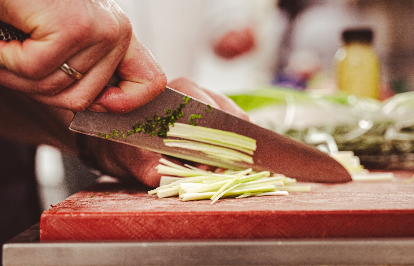 Hand holding a chef knife while slicing vegetables on a red cutting board