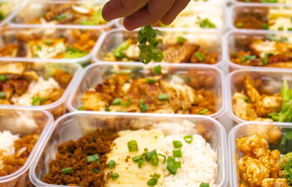 Hand sprinkling green herbs over meal prep containers