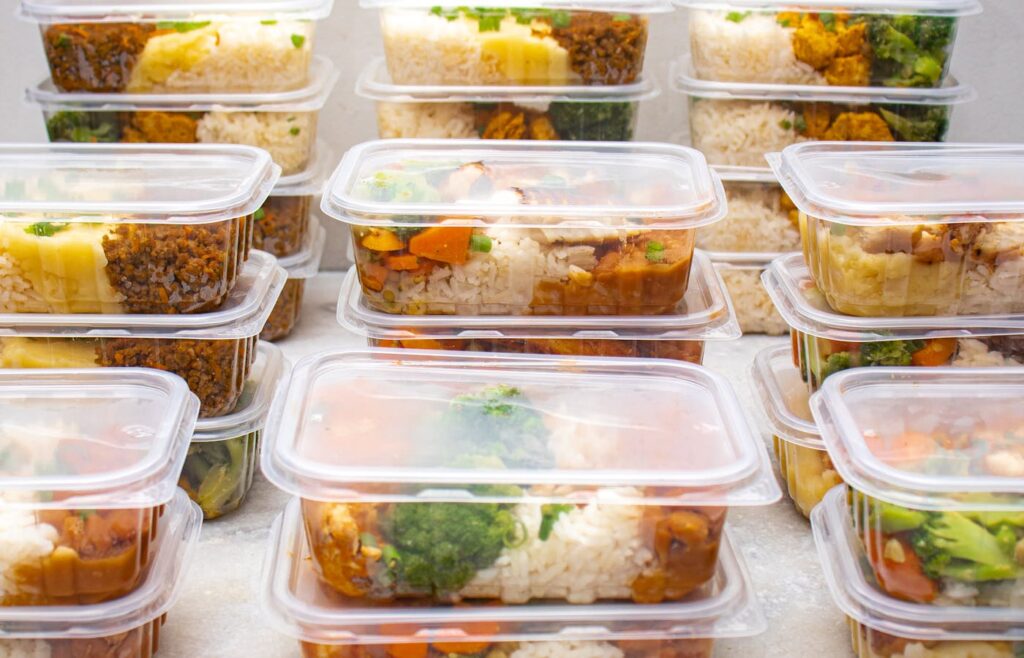 Stacked meal prep containers with rice, vegetables, and cooked protein