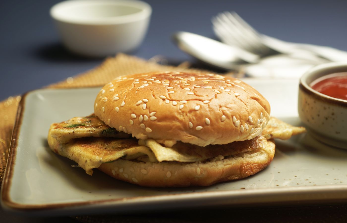 Egg breakfast sandwich on a plate with sauce beside it