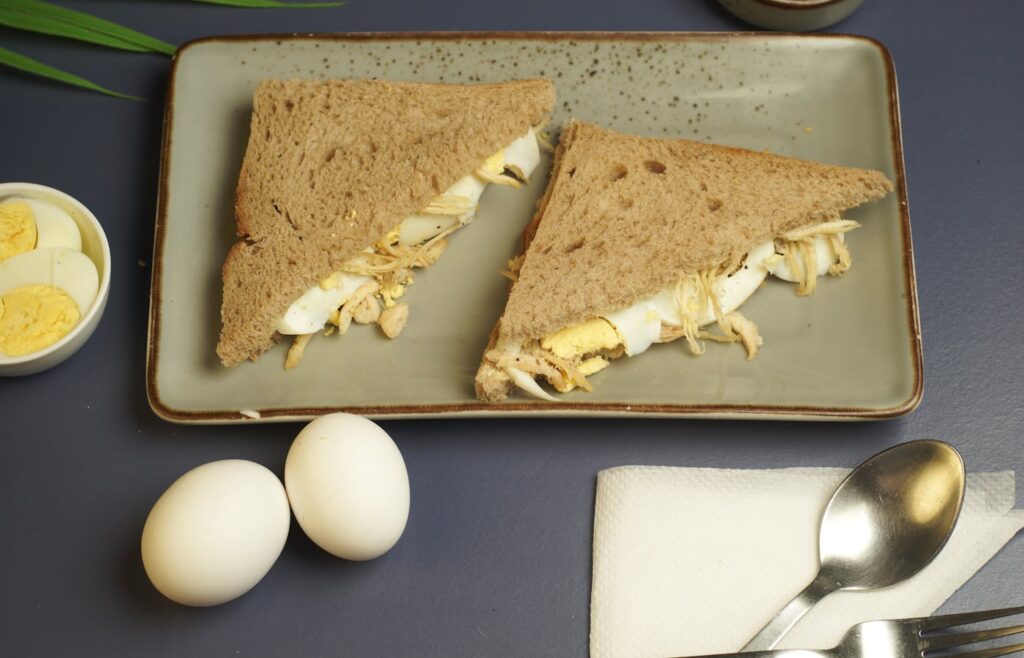 Two egg sandwiches on a plate with boiled eggs beside them