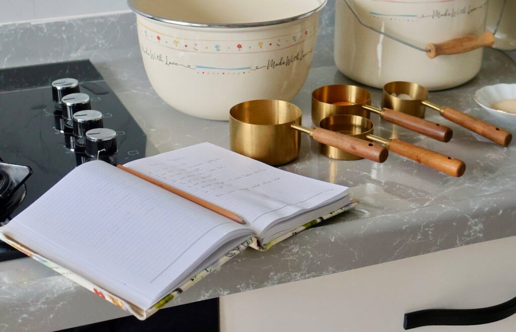 Open recipe notebook beside measuring cups on kitchen counter