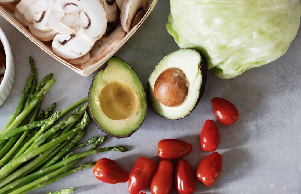 Fresh mushrooms avocado asparagus tomatoes and lettuce on a kitchen counter