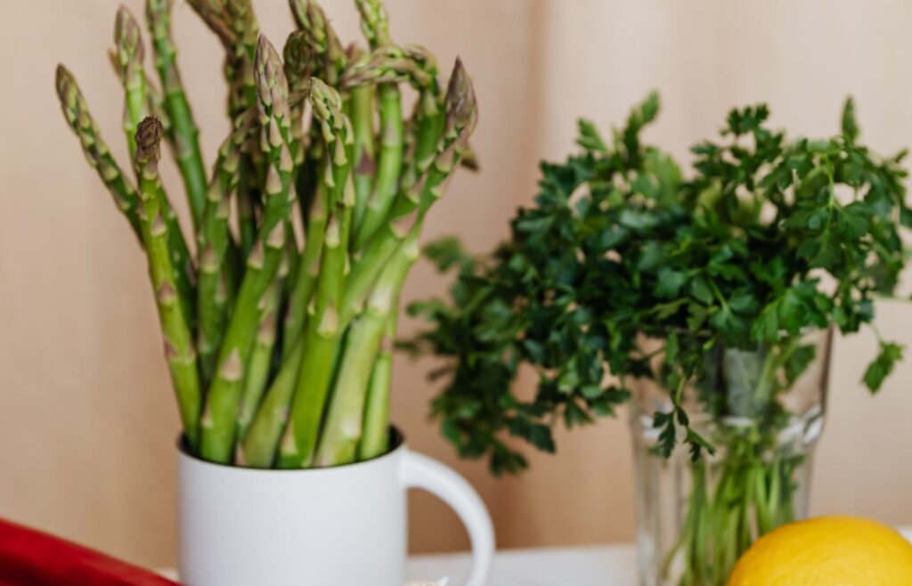 Asparagus, parsley, and herbs standing in cups on a kitchen counter