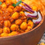 Meatless budget chickpea stew in a brown bowl with red onion, cilantro, and flatbread