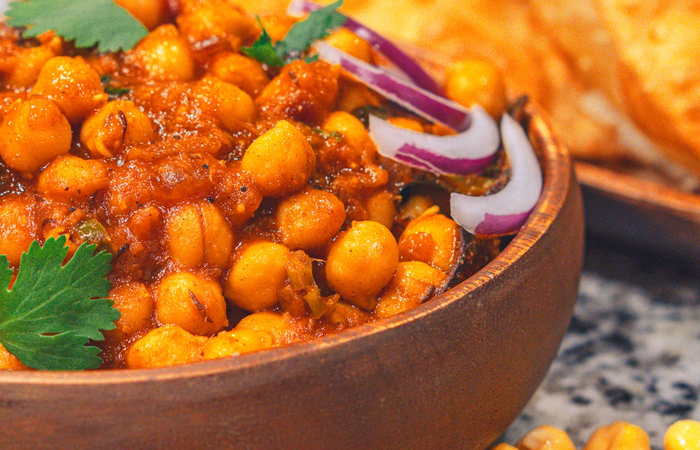 Meatless budget chickpea stew in a brown bowl with red onion, cilantro, and flatbread
