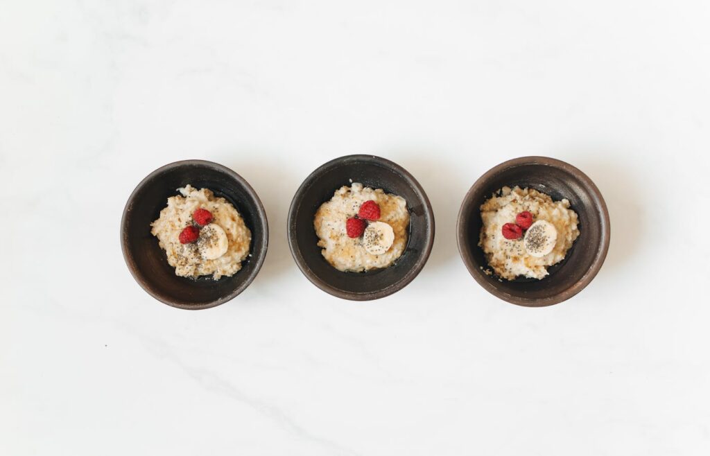 Three small oatmeal bowls with banana raspberries and seeds