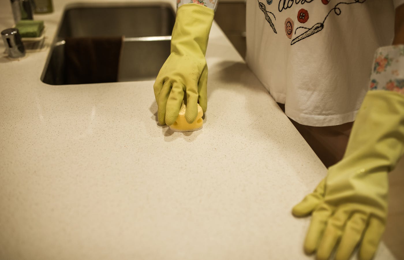 Person wearing yellow gloves wiping a kitchen counter with a sponge