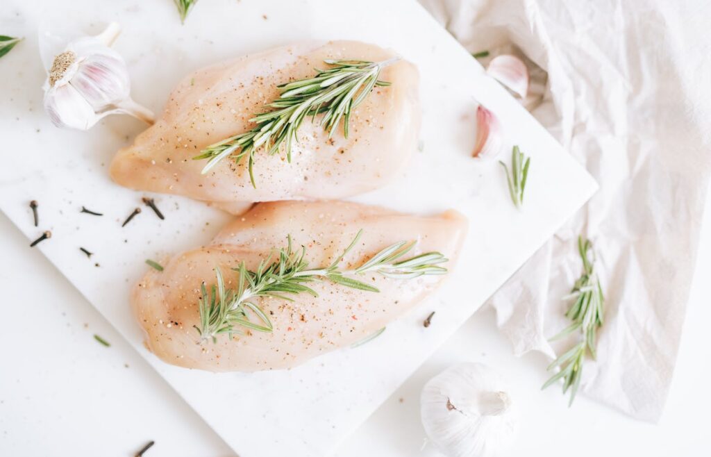 Raw chicken breasts with rosemary and garlic on a white board