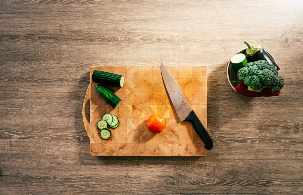 Chef knife on a wooden cutting board with sliced cucumber and vegetables