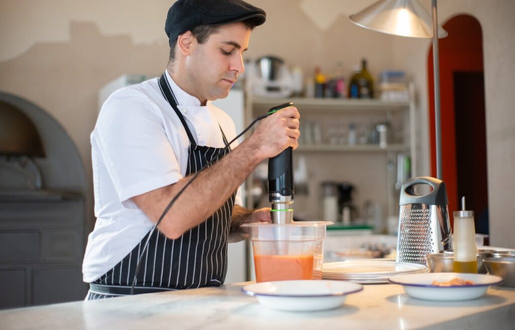 Chef using a hand blender in a container on a kitchen counter