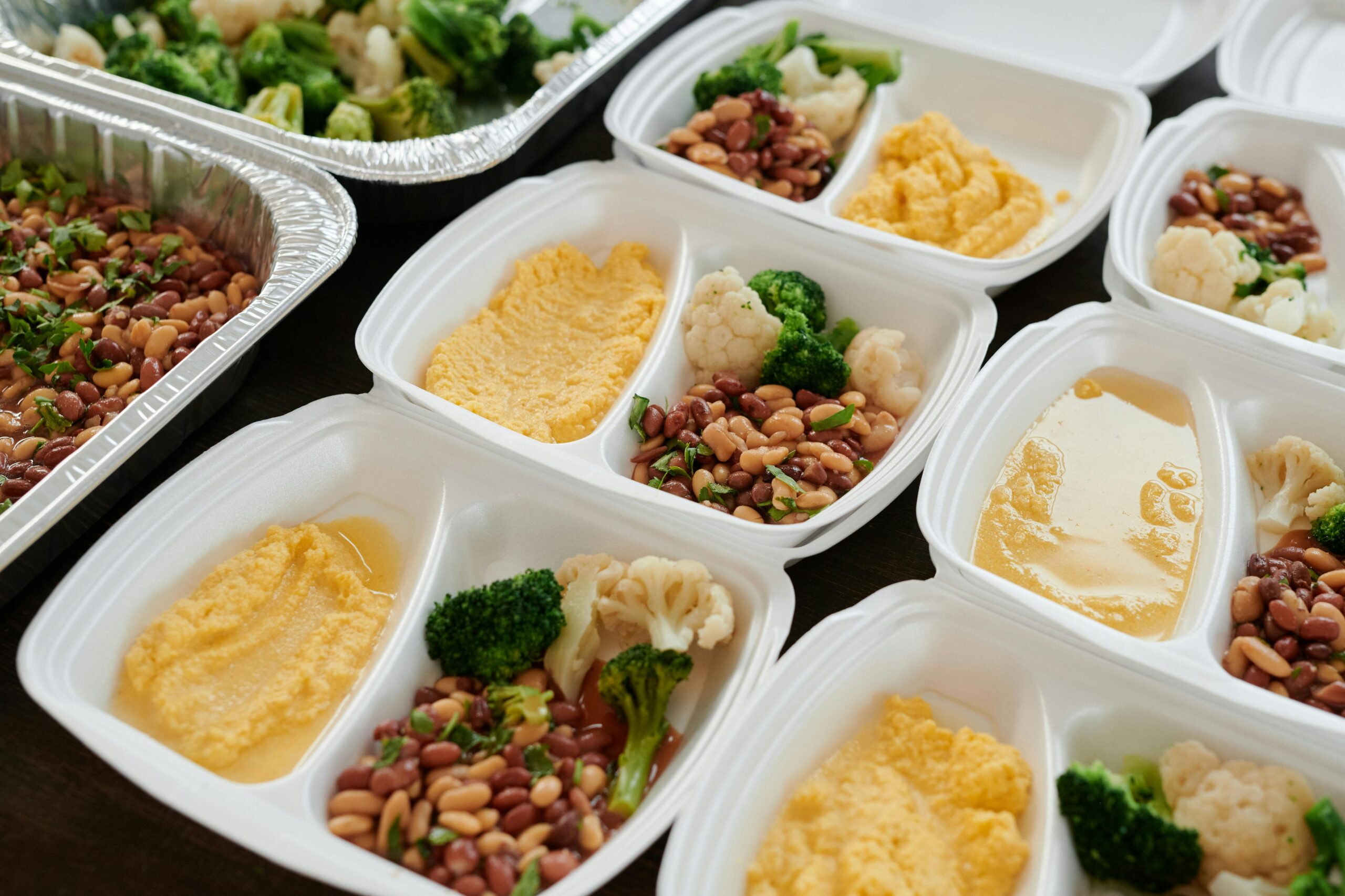 White meal containers filled with beans, broccoli, cauliflower, and polenta