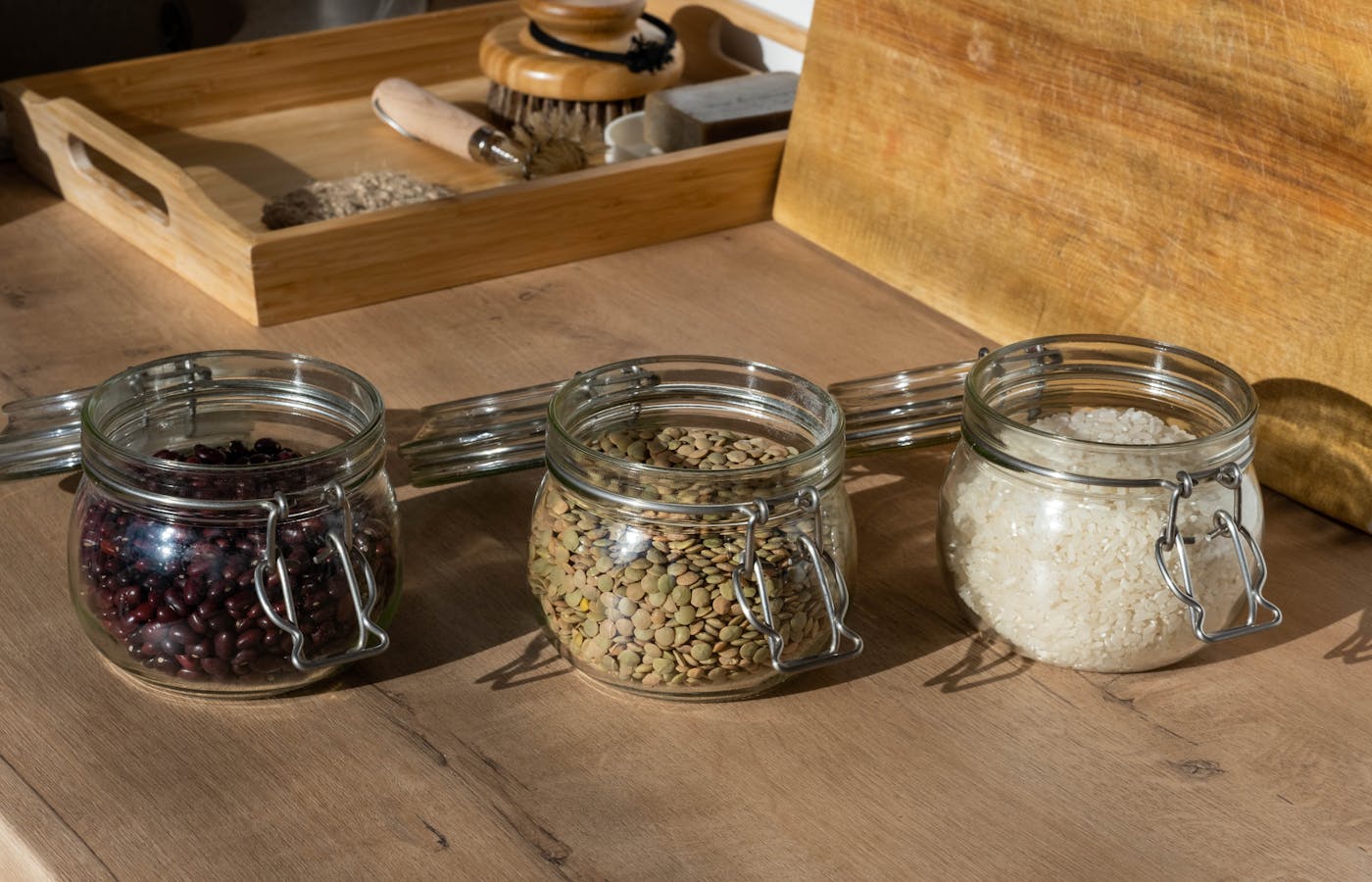 Glass jars of black beans, lentils, and white rice on a wooden kitchen counter