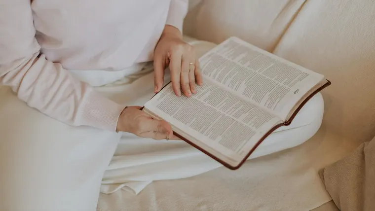 Mulher lendo um livro no sofá, em clima de relaxamento e autocuidado.
