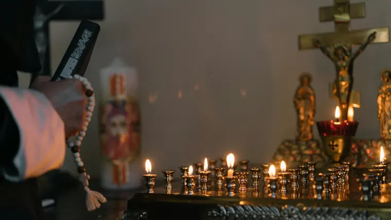 Rosário e vela acesa em oração, com atmosfera de devoção católica.