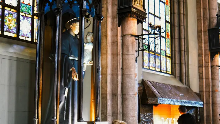 Uma mulher reza diante de uma estátua religiosa dentro de uma catedral ornamentada com vitrais.