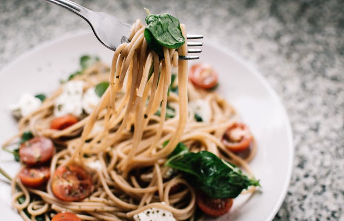 Fork lifting spaghetti with tomatoes and greens from a white plate for quick pasta dinner ideas