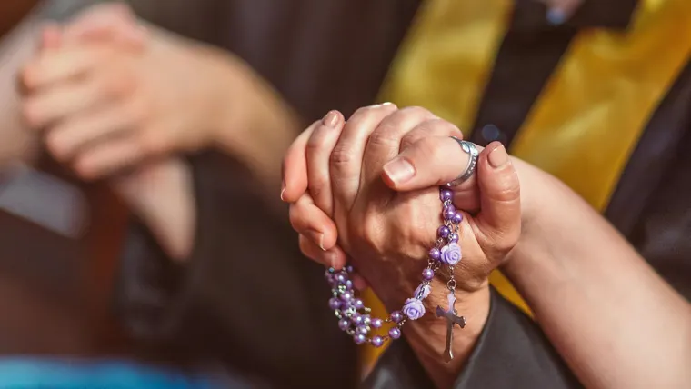 Mãos segurando um terço em oração, com foco religioso e íntimo.