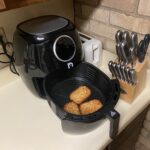 Open black air fryer basket with hash brown patties