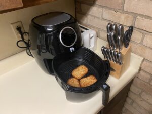 Open black air fryer basket with hash brown patties