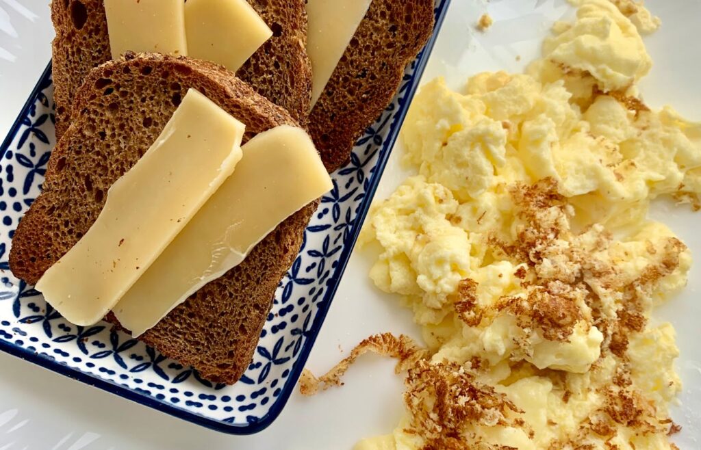 Cheese topped toast with scrambled eggs on a plate